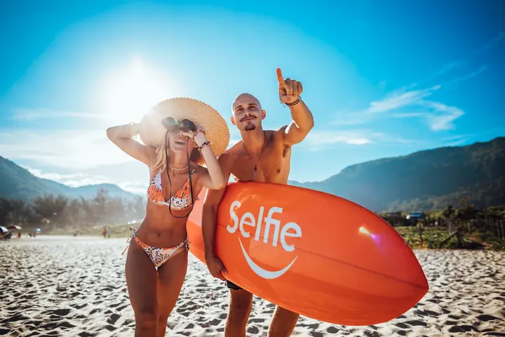 Two models holding a Selfie-branded surfboard on the beach