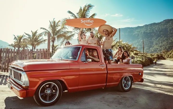 Friends holding a Selfie surfboard in the back of a vintage orange pickup